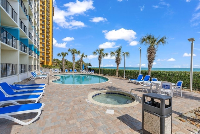 pool with a water view, a hot tub, fence, and a patio