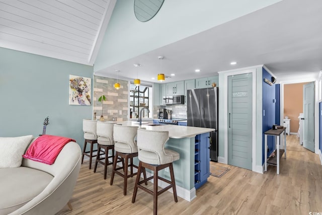 kitchen with light wood-type flooring, a breakfast bar, stainless steel appliances, vaulted ceiling, and decorative light fixtures