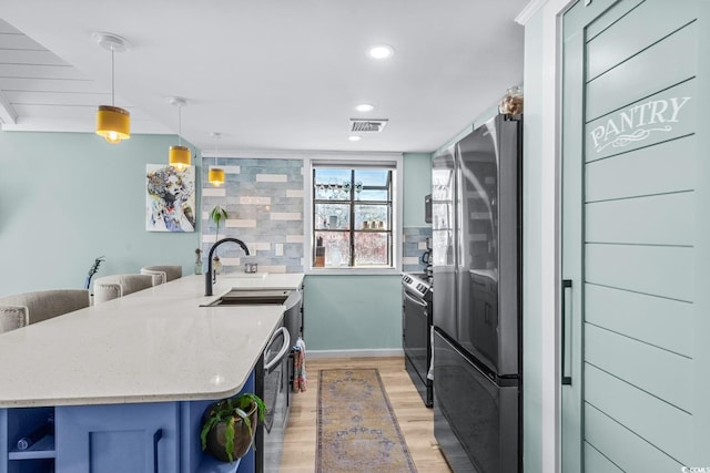 kitchen featuring backsplash, sink, hanging light fixtures, light hardwood / wood-style flooring, and stainless steel appliances