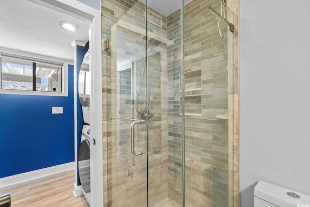 bathroom featuring hardwood / wood-style floors, stacked washing maching and dryer, toilet, and a shower with shower door