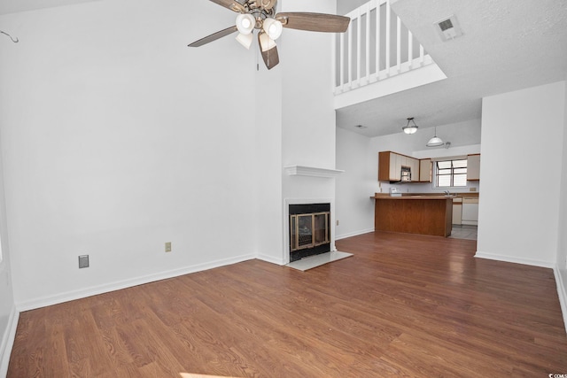 unfurnished living room featuring ceiling fan, wood-type flooring, a textured ceiling, and a high ceiling