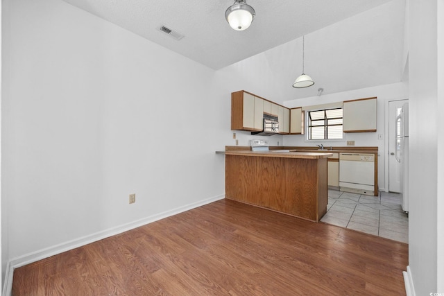 kitchen with kitchen peninsula, pendant lighting, lofted ceiling, light hardwood / wood-style floors, and white appliances