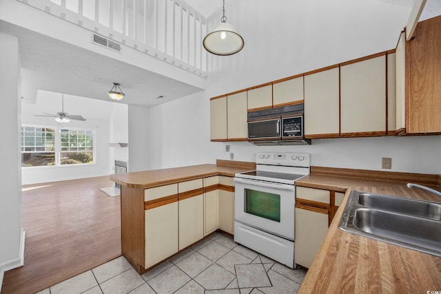 kitchen featuring sink, decorative light fixtures, white range with electric stovetop, light tile patterned flooring, and kitchen peninsula