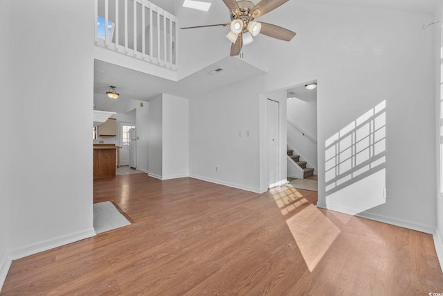 unfurnished living room featuring ceiling fan, a towering ceiling, and light wood-type flooring