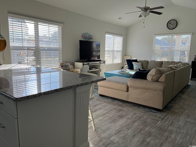 living room featuring ceiling fan, visible vents, vaulted ceiling, and wood finished floors