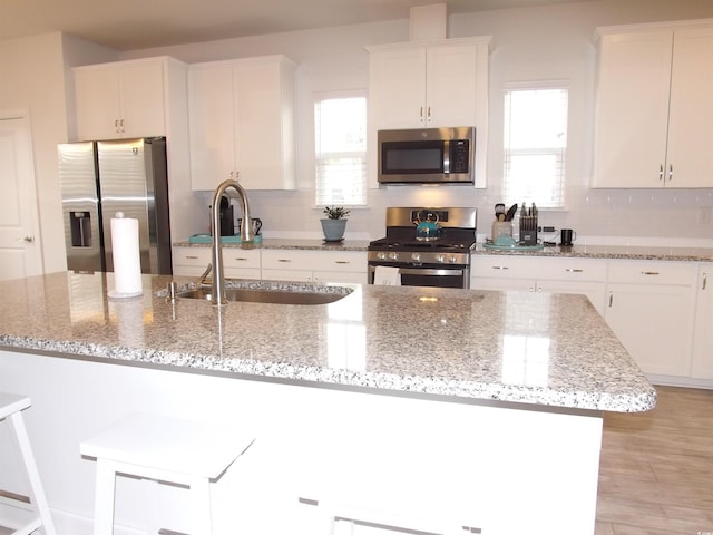 kitchen featuring light stone counters, a center island with sink, appliances with stainless steel finishes, white cabinetry, and a sink