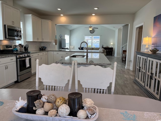 kitchen featuring stainless steel appliances, a sink, white cabinetry, open floor plan, and light stone countertops