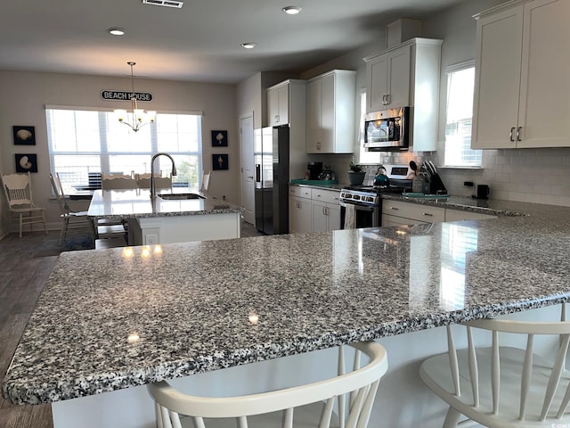 kitchen with a center island with sink, light stone counters, stainless steel appliances, pendant lighting, and a sink