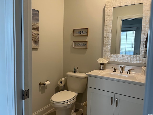 half bath with baseboards, vanity, and toilet