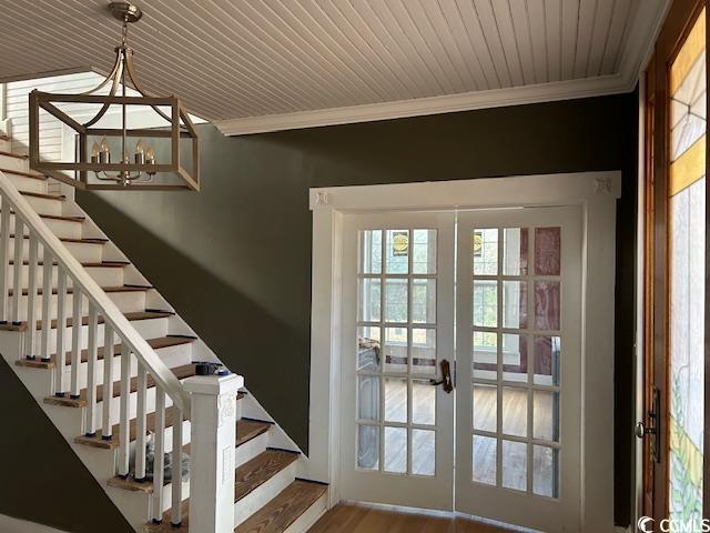 doorway to outside featuring hardwood / wood-style floors, ornamental molding, wood ceiling, an inviting chandelier, and french doors