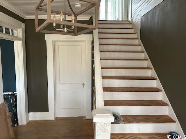 stairway with ornamental molding, hardwood / wood-style floors, and an inviting chandelier