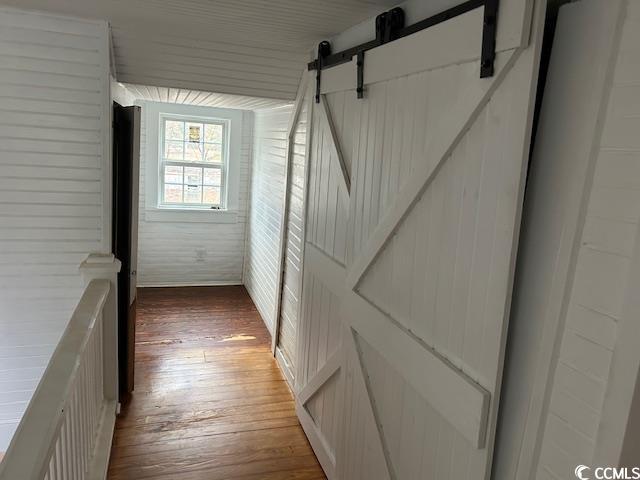 corridor featuring a barn door, wooden walls, and dark hardwood / wood-style flooring