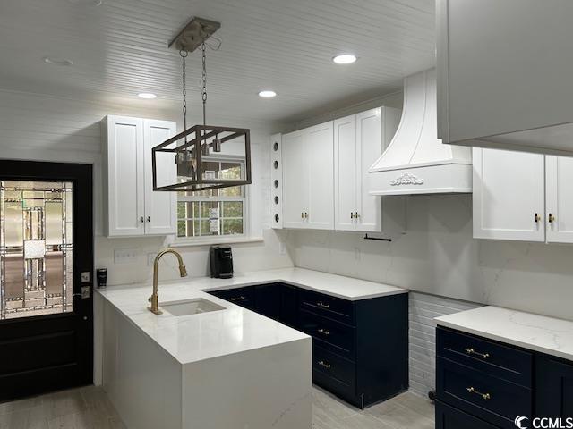 kitchen with sink, decorative light fixtures, custom range hood, light hardwood / wood-style floors, and white cabinets