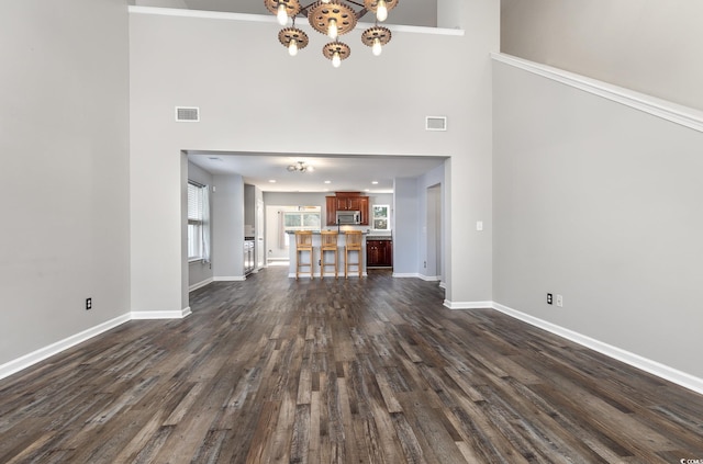 unfurnished living room featuring a towering ceiling, dark hardwood / wood-style floors, crown molding, and a notable chandelier