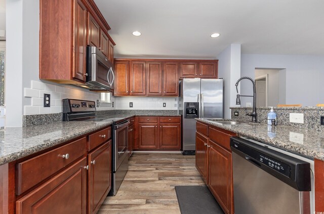 kitchen with light stone counters, stainless steel appliances, light hardwood / wood-style flooring, and sink