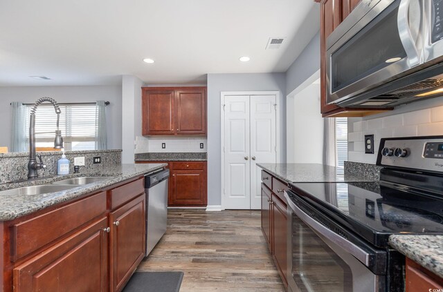 kitchen featuring appliances with stainless steel finishes, backsplash, light stone counters, dark wood-type flooring, and sink