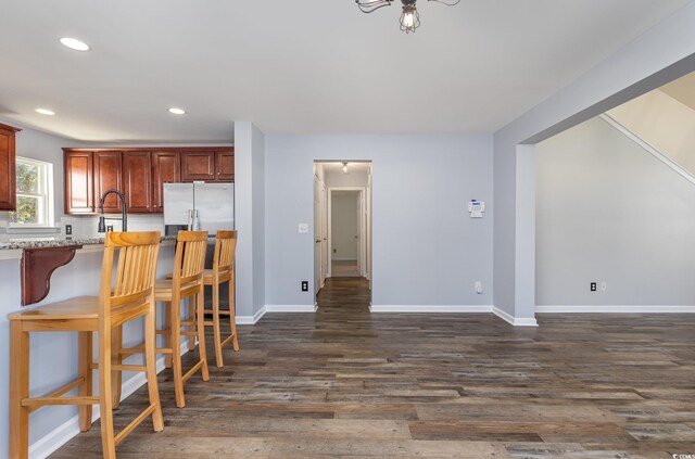 kitchen featuring dark hardwood / wood-style floors, stainless steel fridge, light stone countertops, and a breakfast bar area