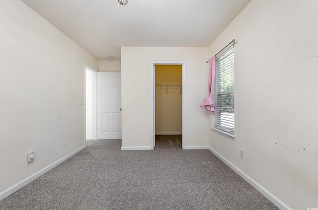 unfurnished bedroom with a walk in closet, light colored carpet, and a closet