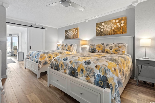 bedroom featuring light hardwood / wood-style flooring, ceiling fan, a barn door, ornamental molding, and a textured ceiling