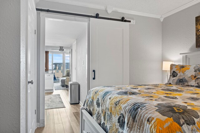 bedroom featuring a textured ceiling, a barn door, light hardwood / wood-style floors, and ornamental molding