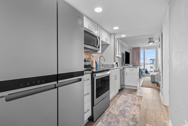 kitchen with decorative backsplash, appliances with stainless steel finishes, sink, light hardwood / wood-style floors, and white cabinetry