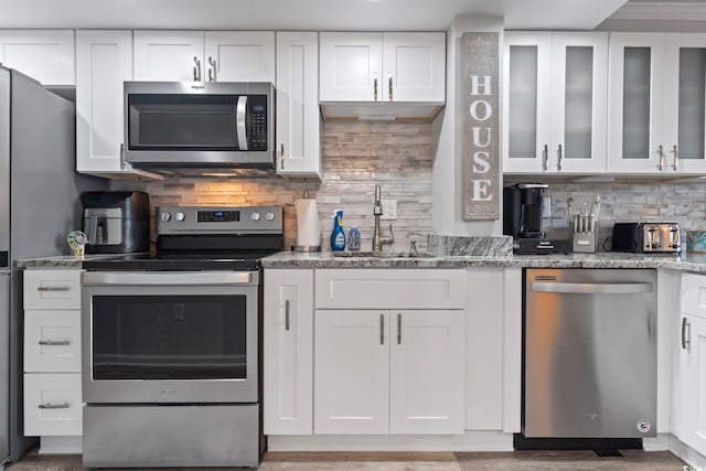 kitchen with tasteful backsplash, light stone countertops, white cabinets, and stainless steel appliances