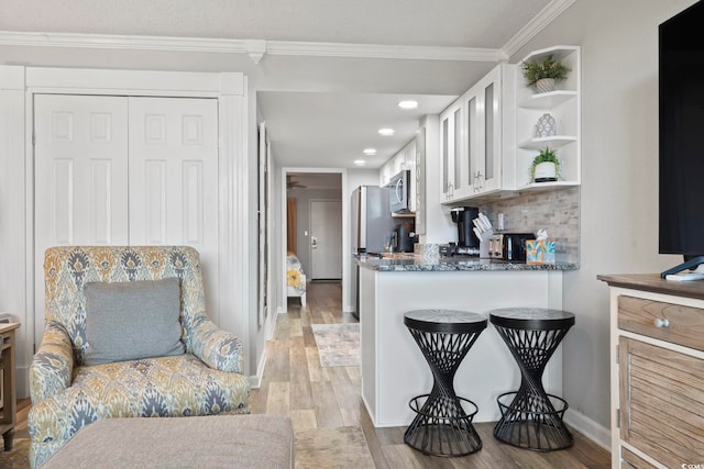 kitchen with backsplash, white cabinets, crown molding, light hardwood / wood-style flooring, and appliances with stainless steel finishes