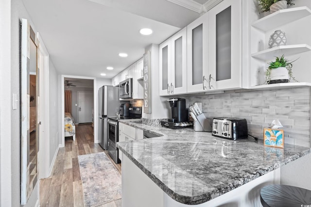 kitchen with kitchen peninsula, backsplash, stainless steel appliances, light hardwood / wood-style flooring, and white cabinetry