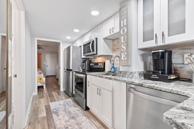 kitchen with light stone countertops, appliances with stainless steel finishes, decorative backsplash, white cabinets, and light wood-type flooring