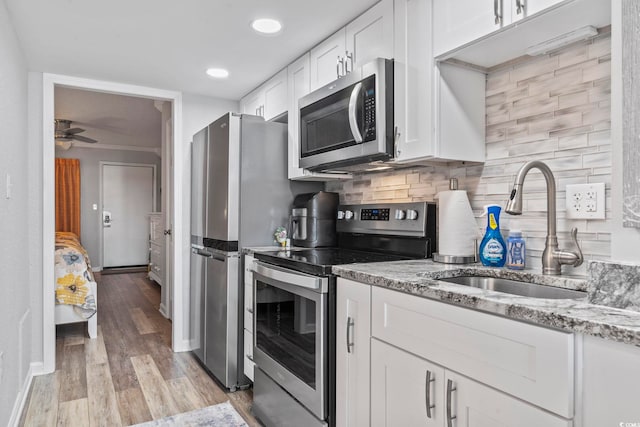 kitchen featuring appliances with stainless steel finishes, backsplash, sink, light hardwood / wood-style floors, and white cabinetry