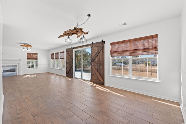 unfurnished living room with a barn door, hardwood / wood-style flooring, and a healthy amount of sunlight