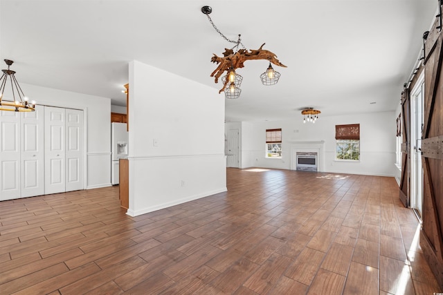 unfurnished living room with a barn door, hardwood / wood-style floors, and a chandelier