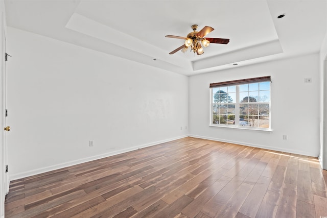 unfurnished room featuring hardwood / wood-style flooring, ceiling fan, and a raised ceiling