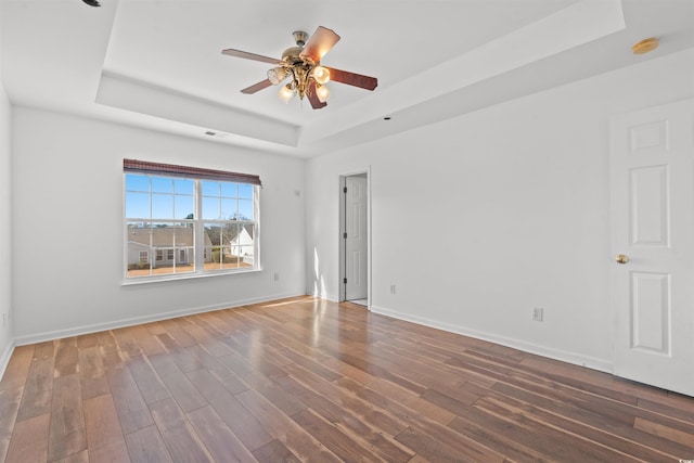 unfurnished room featuring a tray ceiling, ceiling fan, and dark wood-type flooring