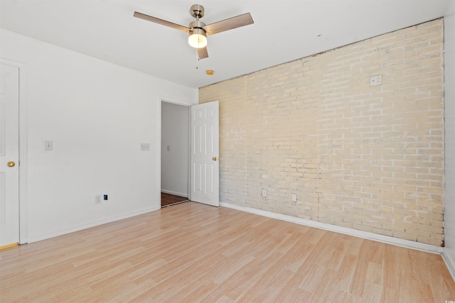 unfurnished room with ceiling fan, light hardwood / wood-style floors, and brick wall