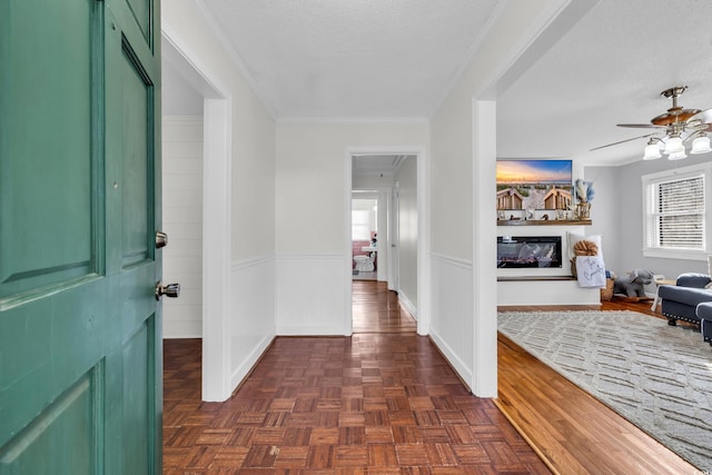 foyer featuring a textured ceiling, a wainscoted wall, a ceiling fan, ornamental molding, and a glass covered fireplace