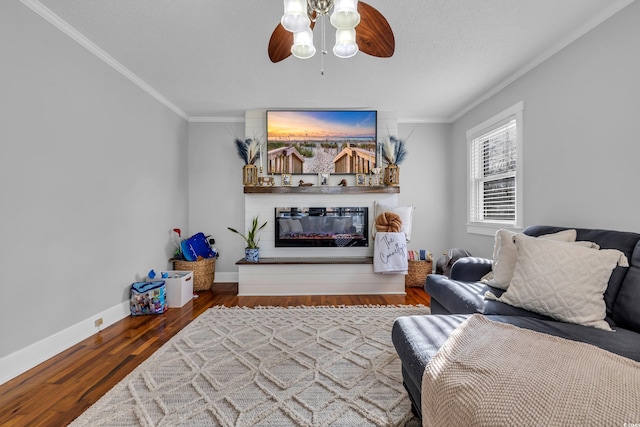 living area with wood finished floors, a ceiling fan, baseboards, a glass covered fireplace, and crown molding