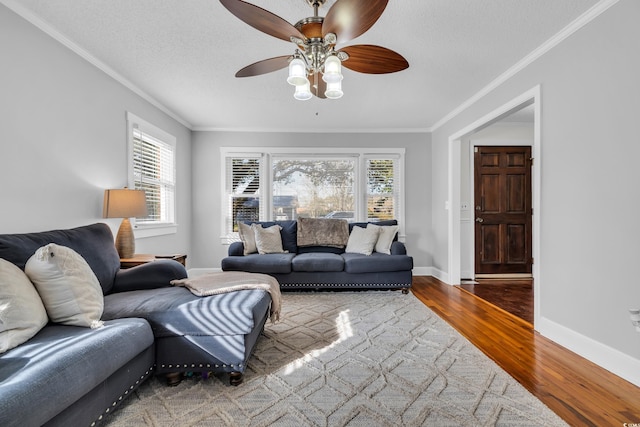 living room featuring ornamental molding, a ceiling fan, a textured ceiling, wood finished floors, and baseboards