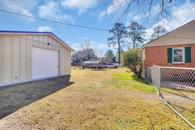 view of yard featuring driveway, a garage, a trampoline, and fence