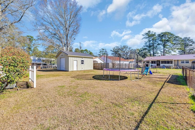 view of yard with a trampoline, a playground, a detached garage, a fenced backyard, and an outdoor structure