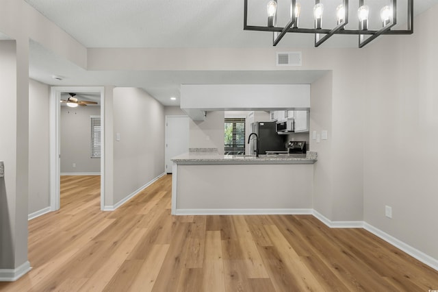 kitchen featuring light stone countertops, ceiling fan with notable chandelier, electric range, light hardwood / wood-style flooring, and white cabinetry