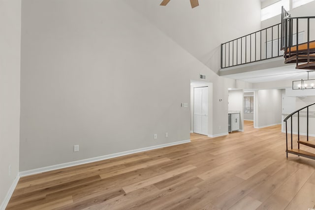 living room featuring light wood-type flooring, a towering ceiling, and ceiling fan with notable chandelier