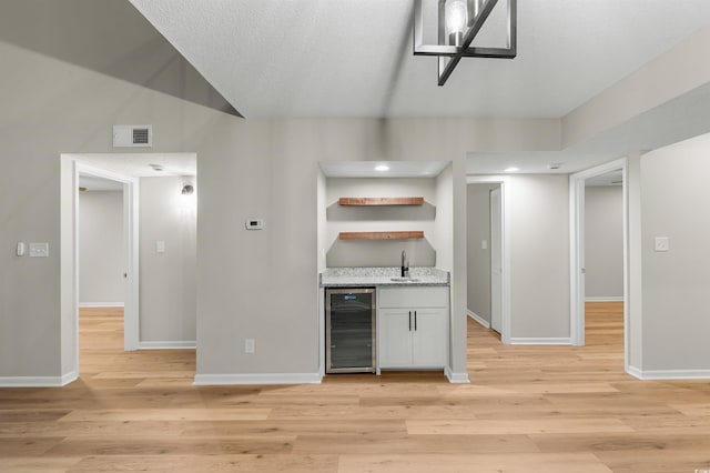 kitchen featuring sink, beverage cooler, light stone counters, light hardwood / wood-style flooring, and white cabinets