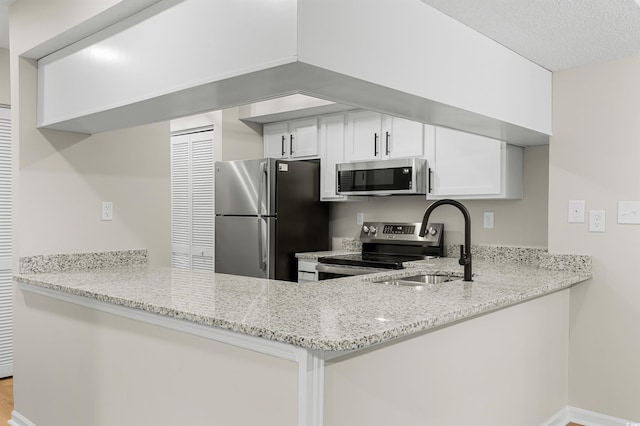 kitchen with sink, light stone counters, white cabinetry, and stainless steel appliances