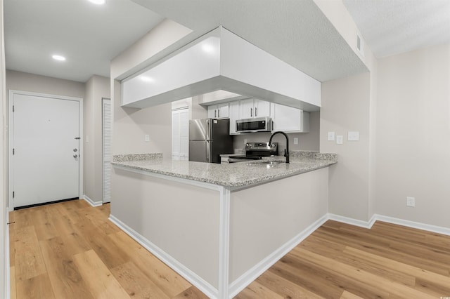 kitchen featuring light stone countertops, light wood-type flooring, stainless steel appliances, sink, and white cabinetry