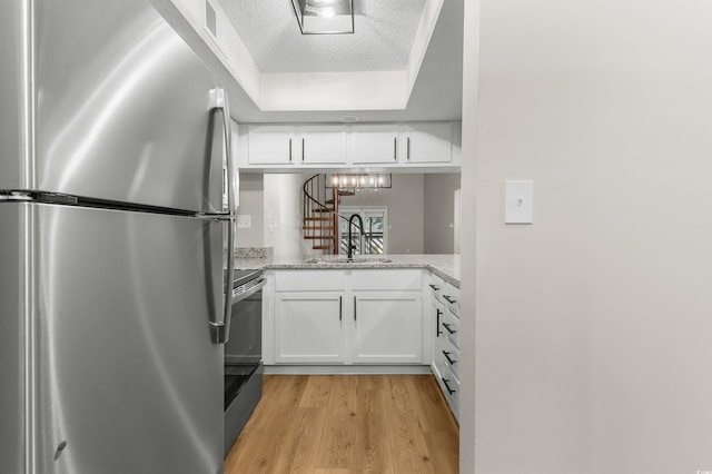 kitchen featuring white cabinets, sink, stainless steel fridge, a textured ceiling, and light stone counters