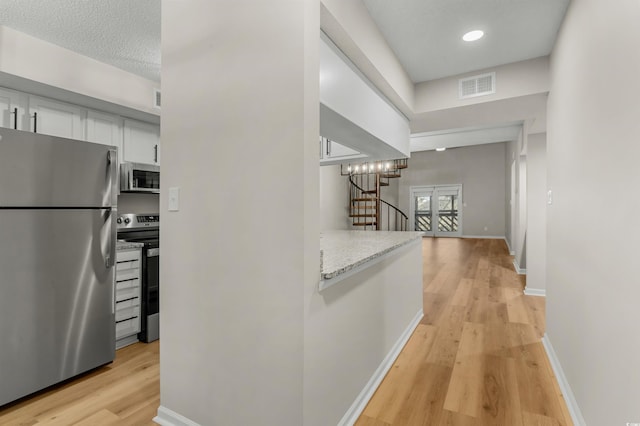 hallway with a textured ceiling, french doors, a notable chandelier, and light wood-type flooring