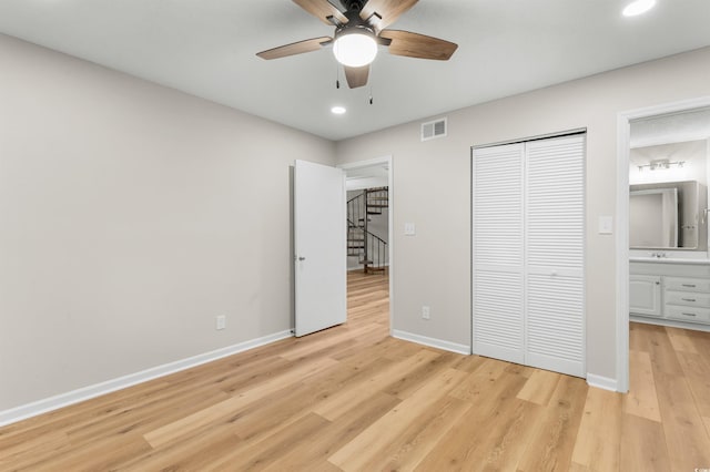 unfurnished bedroom featuring light wood-type flooring, ensuite bathroom, a closet, and ceiling fan