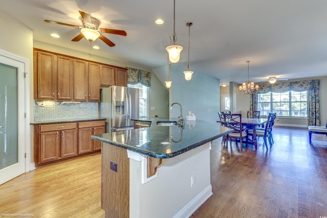 kitchen with a center island with sink, sink, stainless steel fridge, light wood-type flooring, and decorative light fixtures