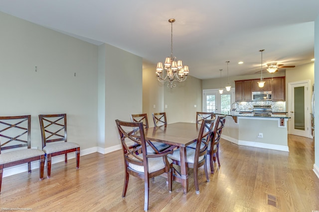 dining room featuring ceiling fan with notable chandelier, light wood-type flooring, and french doors